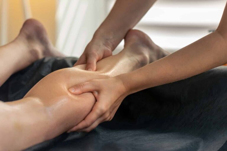 A close-up of a person receiving a relaxing lower leg massage, with the therapist’s hands applying oil and pressure to the calf. The calm setting evokes the soothing atmosphere of a Head, Neck & Shoulders Massage.