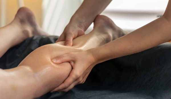 A close-up of a person receiving a relaxing lower leg massage, with the therapist’s hands applying oil and pressure to the calf. The calm setting evokes the soothing atmosphere of a Head, Neck & Shoulders Massage.